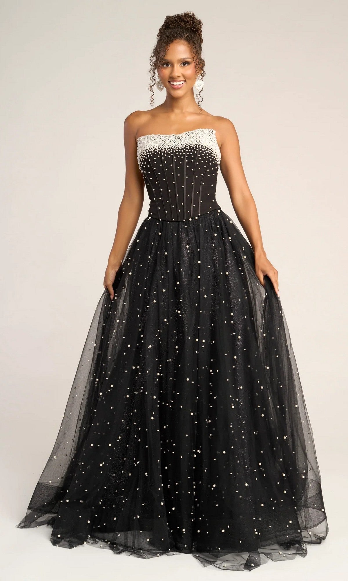 A woman wears the Portia and Scarlett PS26034 long formal dress, a strapless ball gown with a pearl-embellished corset bodice and a full glitter tulle skirt adorned with delicate pearl accents.
